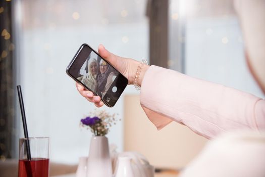 Two Muslim women take a selfie at a table in a cafe, telephoto shot