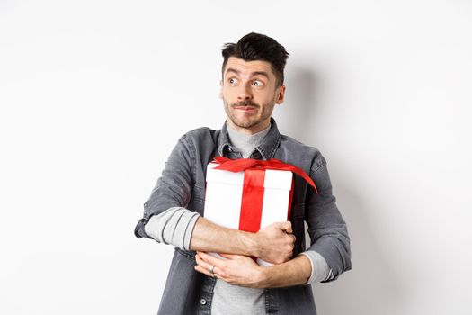 Excited man hugging romantic gift for girlfriend, waiting for valentines date with lover, looking at empty space logo with happy face, standing on white background.