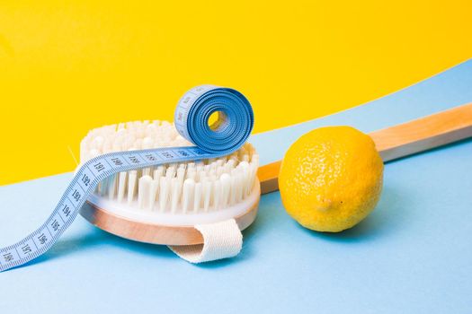 blue measuring tape on a wooden brush with natural pile of cactus and lemon on a yellow and light blue background copy space top view, anti-cellulite massage concept