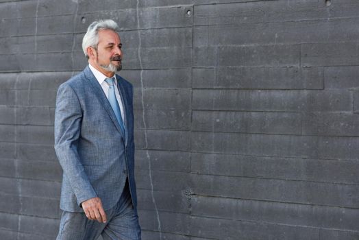 Senior businessman walking outside of modern office building. Successful business man wearing suit and tie in urban background.