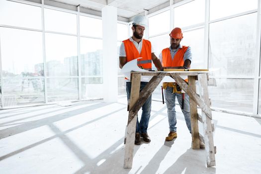 Two young engineers man looking at project plan on the table in construction site