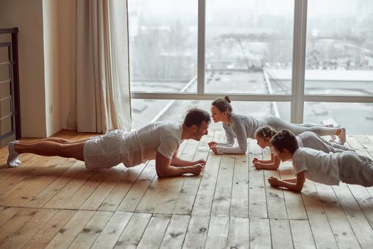 Sporty parents with son and daughter are training core in living room before large window