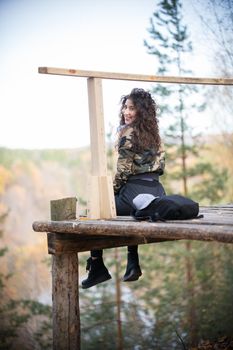 Young woman sitting on a platform on a background of the forest, turns around and smiling. Autumn
