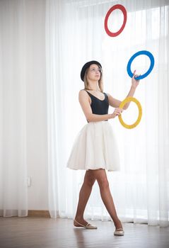 Young woman in a hat juggles with multi-colored rings in the studio, elephoto shot