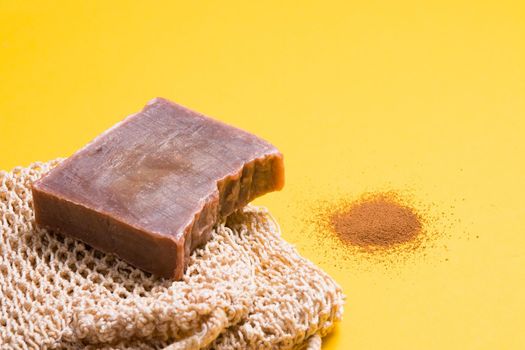 a piece of homemade chocolate soap and a knitted washcloth, a handful of ground coffee on a yellow background, chopped soap with cocoa
