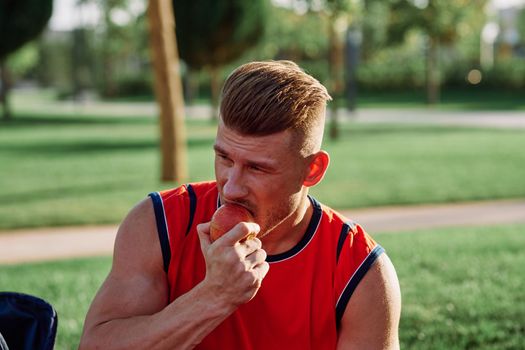 man in the park sits on a bench and eats an apple summer. High quality photo