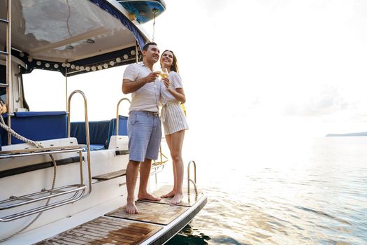 Young loving couple sitting on the yacht deck and drinking wine together