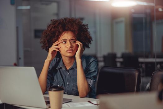 Afro American woman working at her workplace while using laptop and looking away