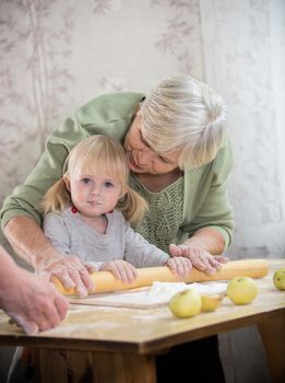 A grandmother making little pies with her granddaughter. Rolling the dough. Mid shot