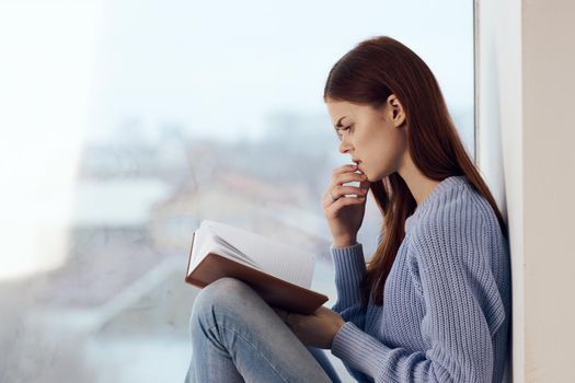 woman reading a book near the window with a cup of drink rest. High quality photo