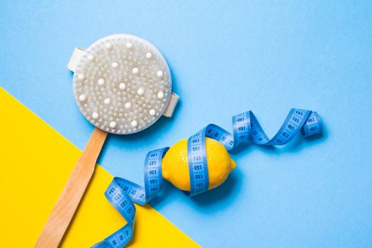 blue measuring tape, wooden brush with natural pile of cactus and lemon on a yellow and light blue background copy space top view, anti-cellulite massage concept