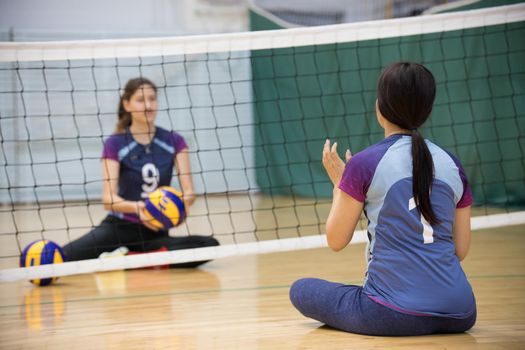 Sports for disabled people. Two young women sitting on the floor and playing volleyball. A woman with ponytail. Mid shot