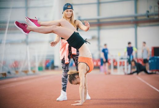 Two young athletic women exercising. Woman standing on her hands and balancing, another woman is ready to catch her. Mid shot