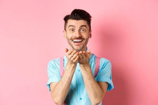 Man in love blowing kiss at camera and smiling passionate, looking at lover happy, enjoying Valentines day, standing over pink background.