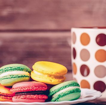 Sweet macaroons dessert of different colors on a plate near the cup.