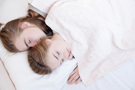 Close-up of a young couple in bed sleeping in an embrace, hiding behind a blanket. The concept of a young family and healthy sleep.
