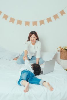 mother with laptop and her child on the bed in the morning