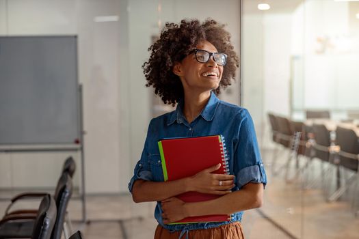 Smiling Afro American lady holding a notebook with documents with two hands in meeting room