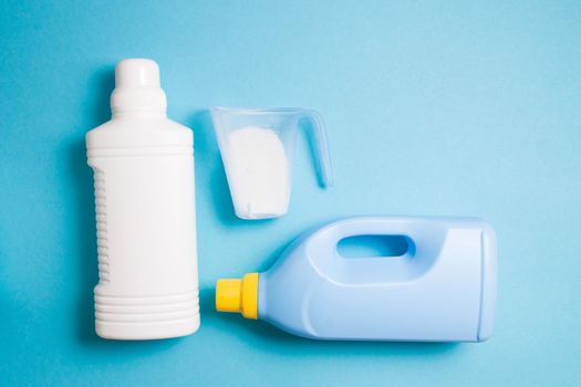 blue plastic bottle with gel for washing children's clothes, a measuring cup with washing powder and a white bottle with bleach against a light blue background, copy space, top view