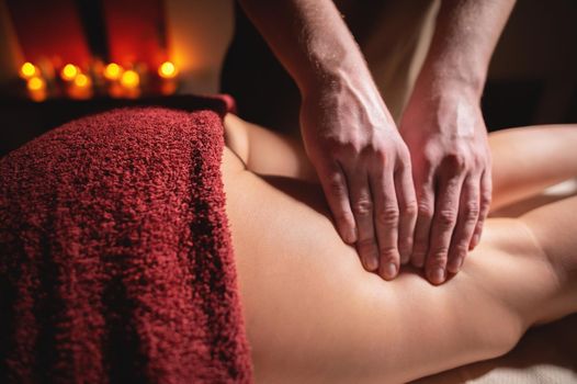 Close-up of premium anti-cellulite thigh massage. Male hands do wellness massage of the thigh to the patient girl in a cozy study with dim light. Luxury massage services.