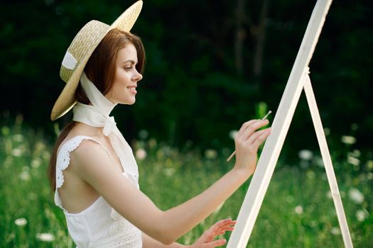 Woman in white dress paints a picture on nature easel. High quality photo