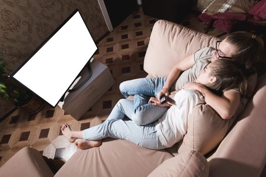 A young seed couple watching a movie while lying on a sofa in the evening in their apartment with a bowl of popcorn. TV screen cut out. Designer blank wide angle.