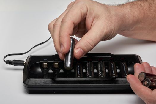 Hands insert AA batteries into black long charger. Close up