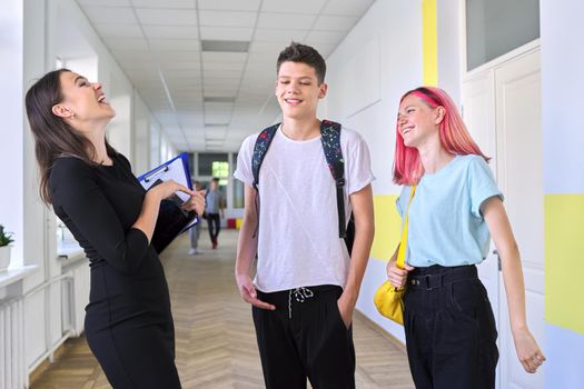 Group of teenage students talking to a female teacher in school corridor, smiling happy people. Teens, youth, school, college concept