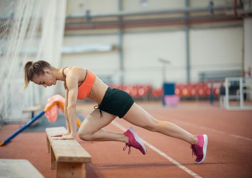 Young athletic woman in sport clothes working out using a bench. Mid shot