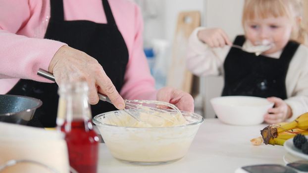 Family making pancakes. A little girl tasting the dough while an old woman making another portion. Mid shot