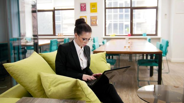 Business concept. A woman sitting on a couch and working with a laptop. Mid shot