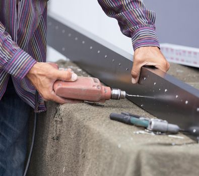 Close up of worker drilling holes in aluminium construction frame with electric drill