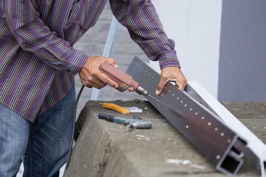 Close up of worker drilling holes in aluminium construction frame with electric drill
