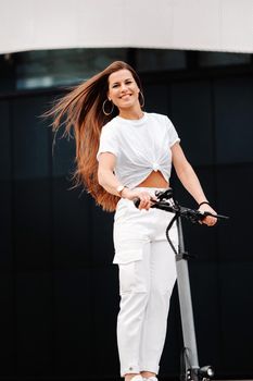 beautiful girl in white stylish clothes on an electric scooter in the city.