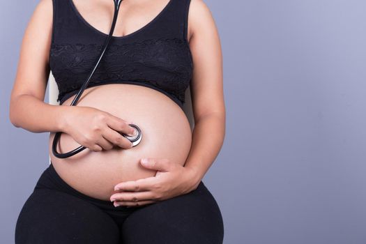 close-up of a pregnant woman with stethoscope listening belly to baby