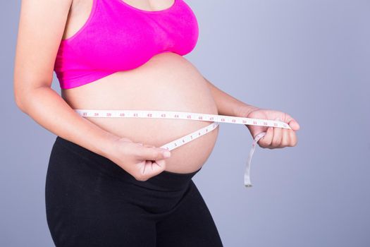 close-up belly of Pregnant woman with measuring tape on gray wall background