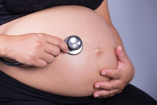 close-up of pregnant woman with stethoscope listening belly to baby