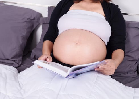 close up pregnant woman reading a book while lying on a bed in the bedroom at home