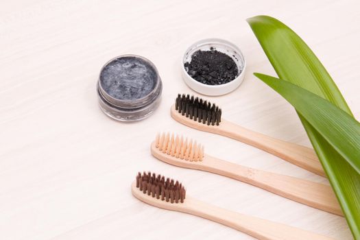 bamboo toothbrushes on a wooden table, homemade charcoal toothpaste in a small glass jar, leaves long plants, eco friendly life style concept, zero waste