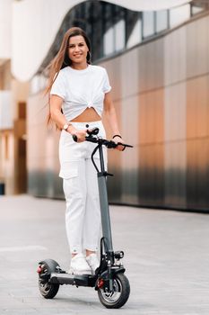 beautiful girl in white stylish clothes on an electric scooter in the city.