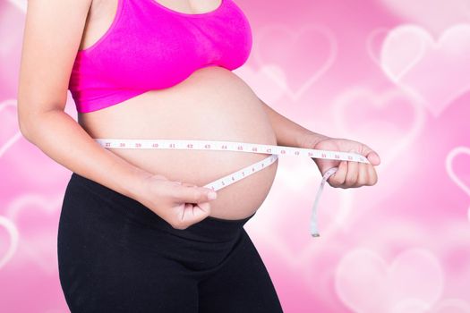 close-up belly of Pregnant woman with measuring tape on heart background