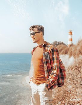 Stylish young handsome man standing on coast and enjoying view of sea.