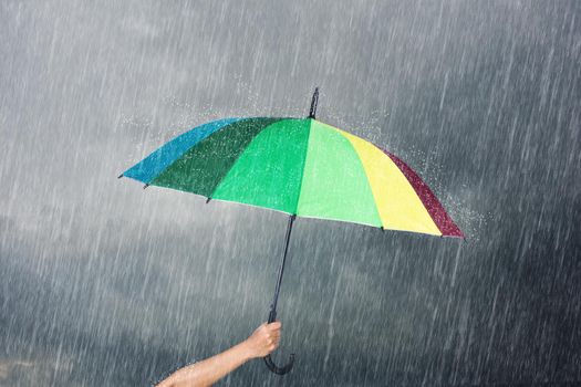 hand holding multicolored umbrella under dark sky with falling rain