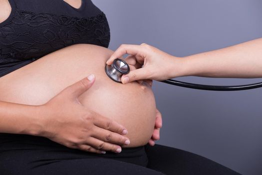 Belly closeup of a pregnant woman examined with a stethoscope