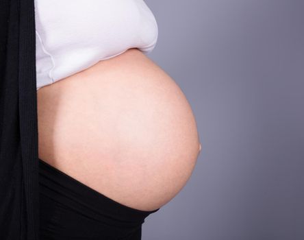 Close-up of pregnant woman belly on gray wall background