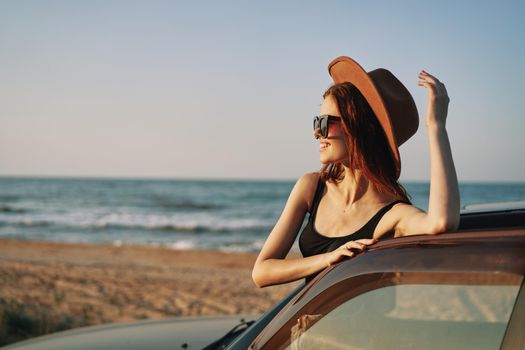 cheerful woman in sunglasses and a hat on the ocean near the car. High quality photo