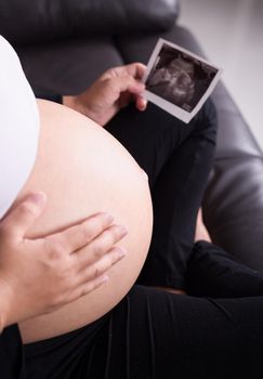 close up pregnant woman sitting on sofa and holding her child ultrasound picture