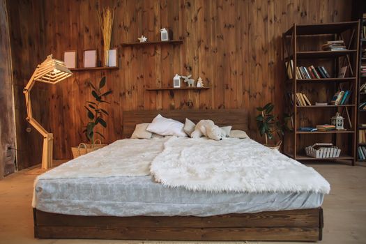 Bright interior of the bedroom with wooden wall, a wooden bed with white, loft interior with decorative lamp and book shelves in studio