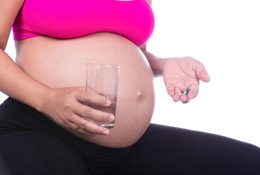 Close-up of pregnant woman hand with glass of water and pill isolated on whie background