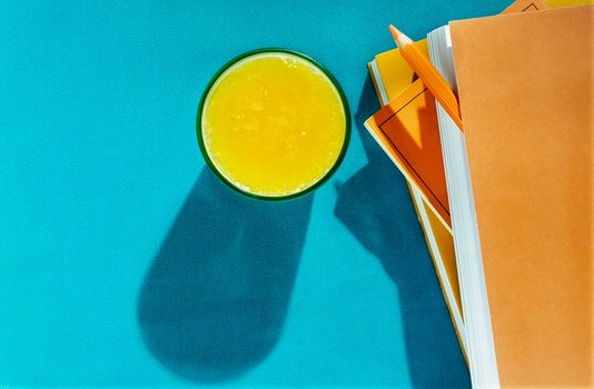 Fresh orange juice in blue glass on blue background , books with orange covers and one orange pencil , 